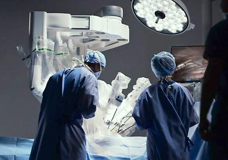 people dressed in surgical scrubs are shown from behind in a bright operating room